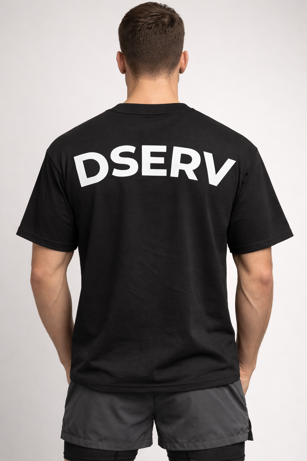 Person wearing a black t-shirt with 'DSERV' printed on the back against a light gray background