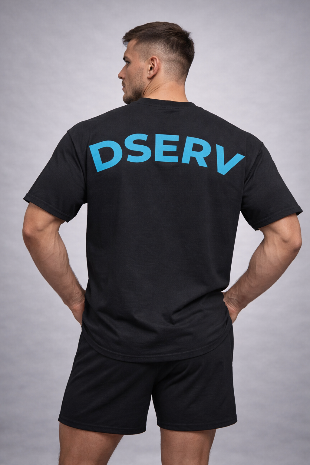 Man wearing a black t-shirt with 'DSERV' printed on the back against a gray background