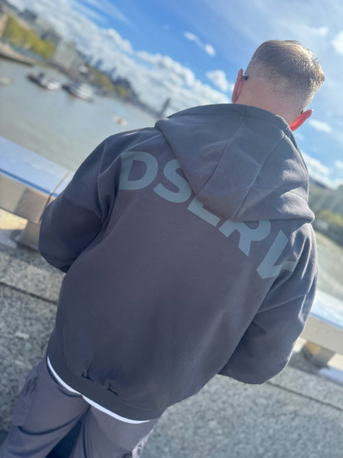 Person wearing a hoodie with 'DSERV' branding, standing by a waterfront.