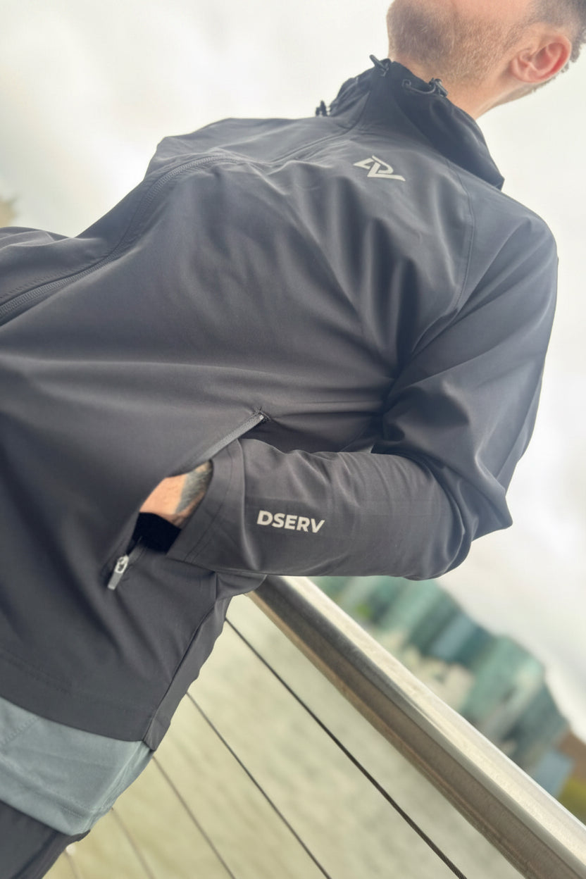 Person wearing a gray jacket with 'Dserv' branding, standing outdoors.